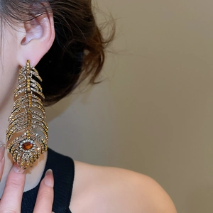 Close-up of luxury gold feather earrings with yellow rhinestones and orange gemstones