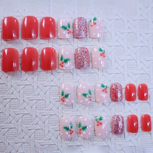Christmas press-on nails with red berry patterns and silver glitter on white texture