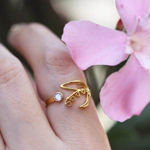 Macro shot of gold leaf ring with light purple zircon on finger against a soft flower