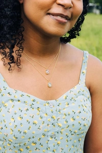 Detail of layered gold necklaces with purple heart and green leaf pendants on a model