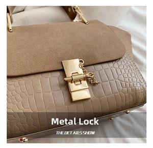 Close-up of golden metal clasp on khaki crocodile embossed leather and brown suede bag