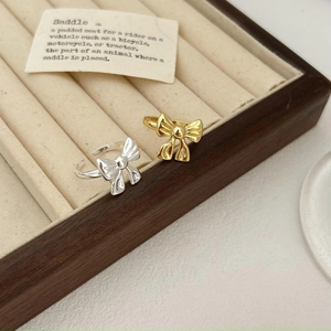 Minimalist bow-shaped rings in gold and silver finish displayed on a jewelry cushion