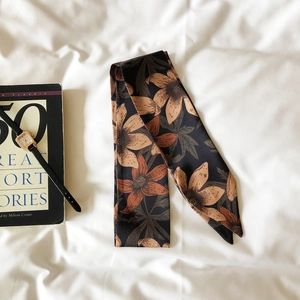Detail view of vintage floral silk scarf styled with book and watch on textured fabric