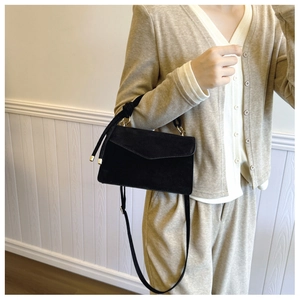 Model showcasing a black suede crossbody bag with gold hardware and removable shoulder strap