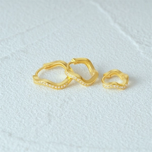 Detail view of wavy square gold earrings with sparkling zircon stones on textured surface