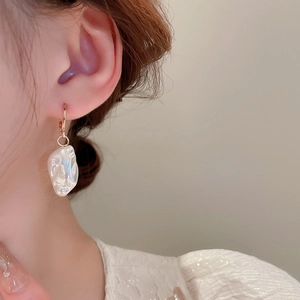Dettaglio dell'orecchino con perla irregolare su modella con elegante design dorato