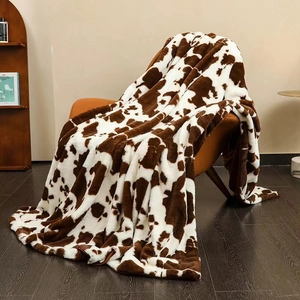 Cosy brown and white cow print faux rabbit fur blanket draped over a leather sofa chair