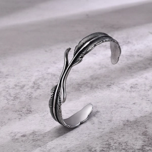 Detailed close-up of vintage silver feather pattern on a stainless steel open cuff bracelet