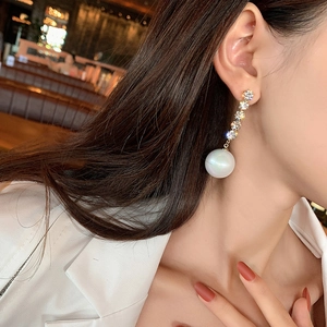 Close-up of elegant gold drop earrings with vertical rhinestones and a large white pearl