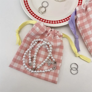 Flat lay of pink checkered drawstring pouches with pearl necklace and silver rings