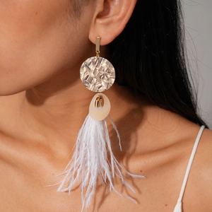 Close-up of golden disk earrings with resin links and white feather tassels on a model