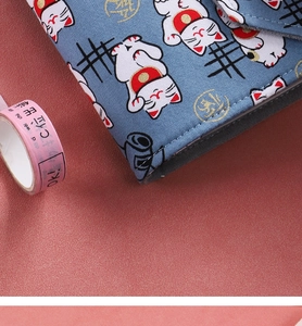 Close-up of blue fabric notebook cover with white lucky cat pattern and gold characters