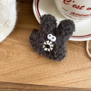 Close-up of cute dark grey plush bunny hair clip with white eyes on wood surface