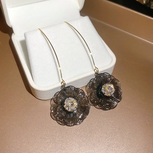 Détail de boucles d'oreilles longues dorées 18K avec pétales noirs et zircones