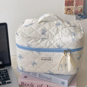 Beauty case trapuntato con fiori blu e nastri su sfondo di libri color pastello