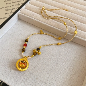 Detailed close-up of gold Daruma pendant with pearls and woven rope on jewelry tray