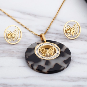 Golden butterfly necklace and earrings set with tortoiseshell resin on marble backdrop