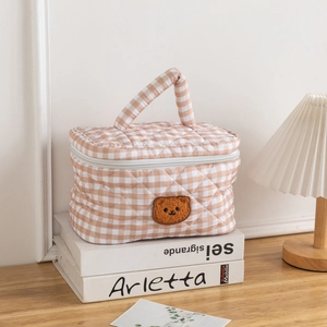 Detailed close-up of quilted gingham bear makeup bag on white books with lamp