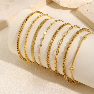 Set of eight gold layered snake and twist chain bracelets on a minimalist white stand