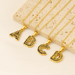 Golden bark texture alphabet pendant necklaces A-D on natural stone display
