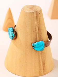 Detail view of a vintage bronze cuff bracelet with turquoise stones on a wooden stand
