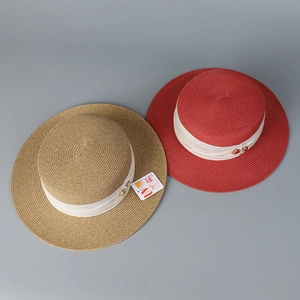 Detail of flat top straw hats in khaki and red with UV protection and ribbon trim