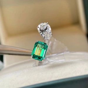 Silver open ring with emerald cut green gem and pear shaped clear stone on velvet