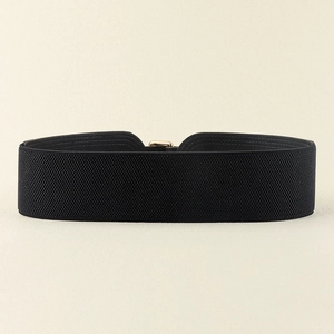 Detail of black elastic wide belt featuring a polished gold square metal buckle