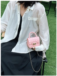 Detailed close-up of pink quilted jelly bag with golden chain strap on green grass