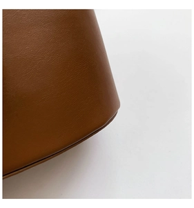 Detailed macro view of the premium brown leather texture and rounded base of the bucket bag
