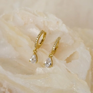 Close-up of gold pear-shaped drop earrings with sparkling pavé hoops on natural stone