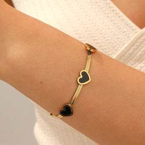Gold-plated flat blade chain bracelet with black heart charms worn on a woman's wrist