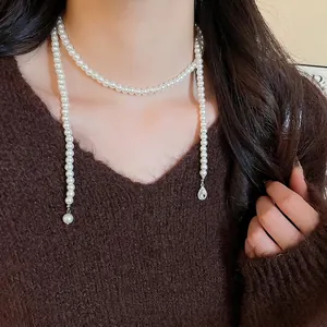 Elegant long pearl strand necklace with a teardrop crystal pendant worn over a sweater