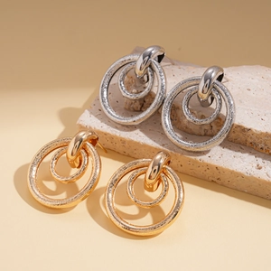 Detail of matte gold and silver geometric hollow earrings on a textured stone base