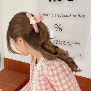 Detail of a pink plush hair claw clip with cream heart accent on brown wavy hair