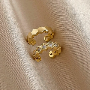 Close-up of gold-plated C-shaped ear cuffs with honeycomb patterns on champagne silk