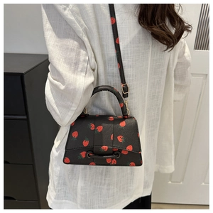 Zwarte handtas met aardbeienprint en verstelbare riem getoond op een model outfit
