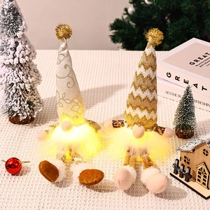 Close-up of glowing Christmas gnomes with golden knit hats and warm LED lights