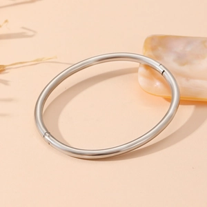 Close-up of polished silver stainless steel oval bangle on a natural beige background