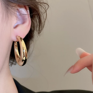 Gros plan détaillé d'une grande créole dorée polie portée par un mannequin pour un look chic