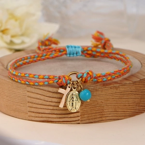 Braided rope bracelet with cross pendant and blue bead on wooden stand