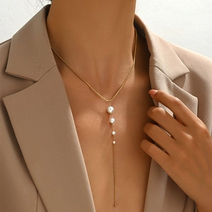 Vintage style gold snake chain necklace with elegant white pearl tassels on beige blazer
