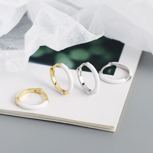 Close-up of gold and silver S925 earrings with white enamel finish on wrinkled paper