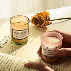 Detailed view of handmade soy candles in glass jars with dry rose and open book backdrop