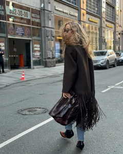 Close-up of a brown wool coat featuring long tassels on the hem with a crocodile texture bag
