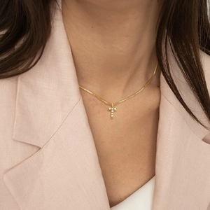 Detalle de collar con colgante de letra T dorada y cadena de caja usado por una modelo