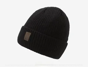 Detail of black ribbed knit beanie with brown leather patch on light gray background