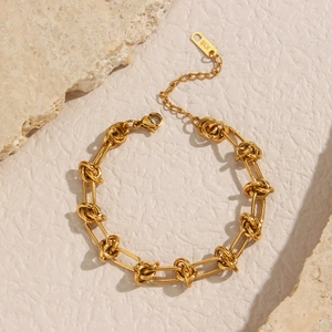 Macro shot of gold knotted chain bracelet with K18 tag on light natural stone background