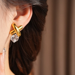 Close-up of vintage gold cross earrings with clear geometric crystals worn by model