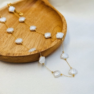 Detailed view of the fan-shaped shell pendants and golden chain on a wooden base